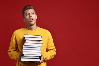 Photo of Tired student with stack of books having stress before exam on red background. Space for text