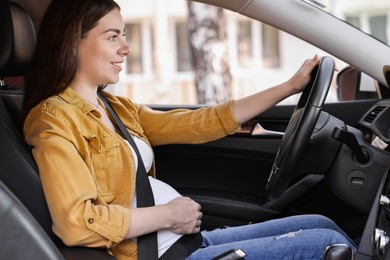 Photo of Smiling pregnant woman with safety belt driving car