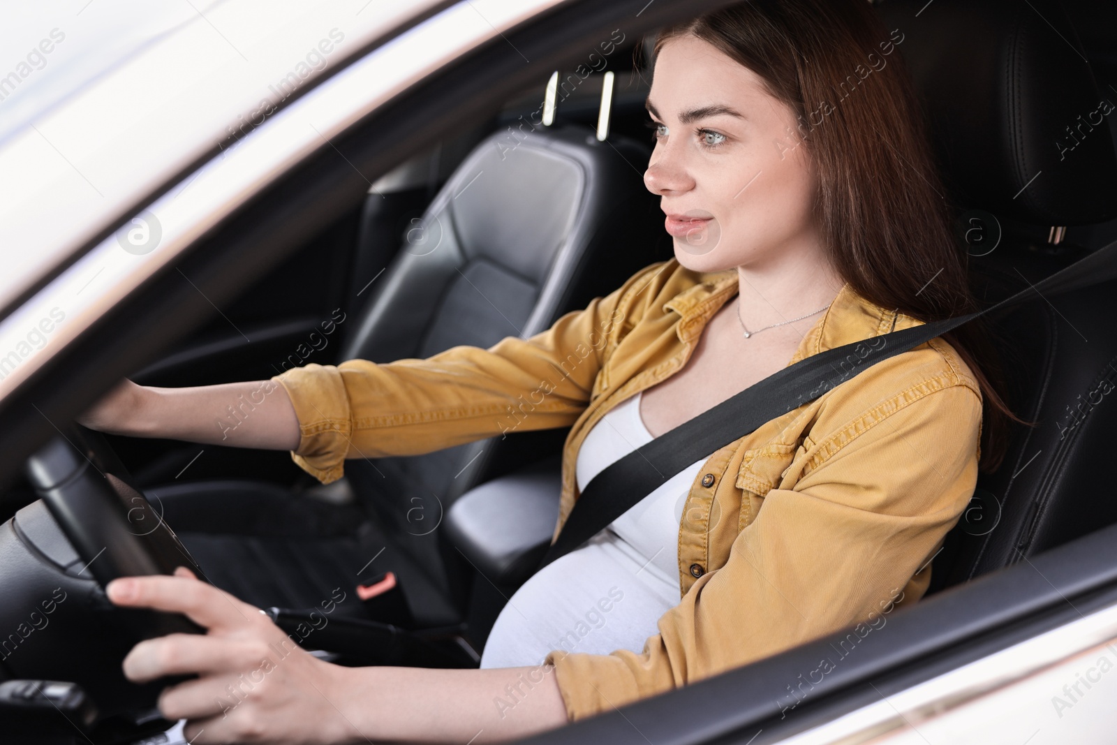 Photo of Pregnant woman with safety belt driving car, view from outside