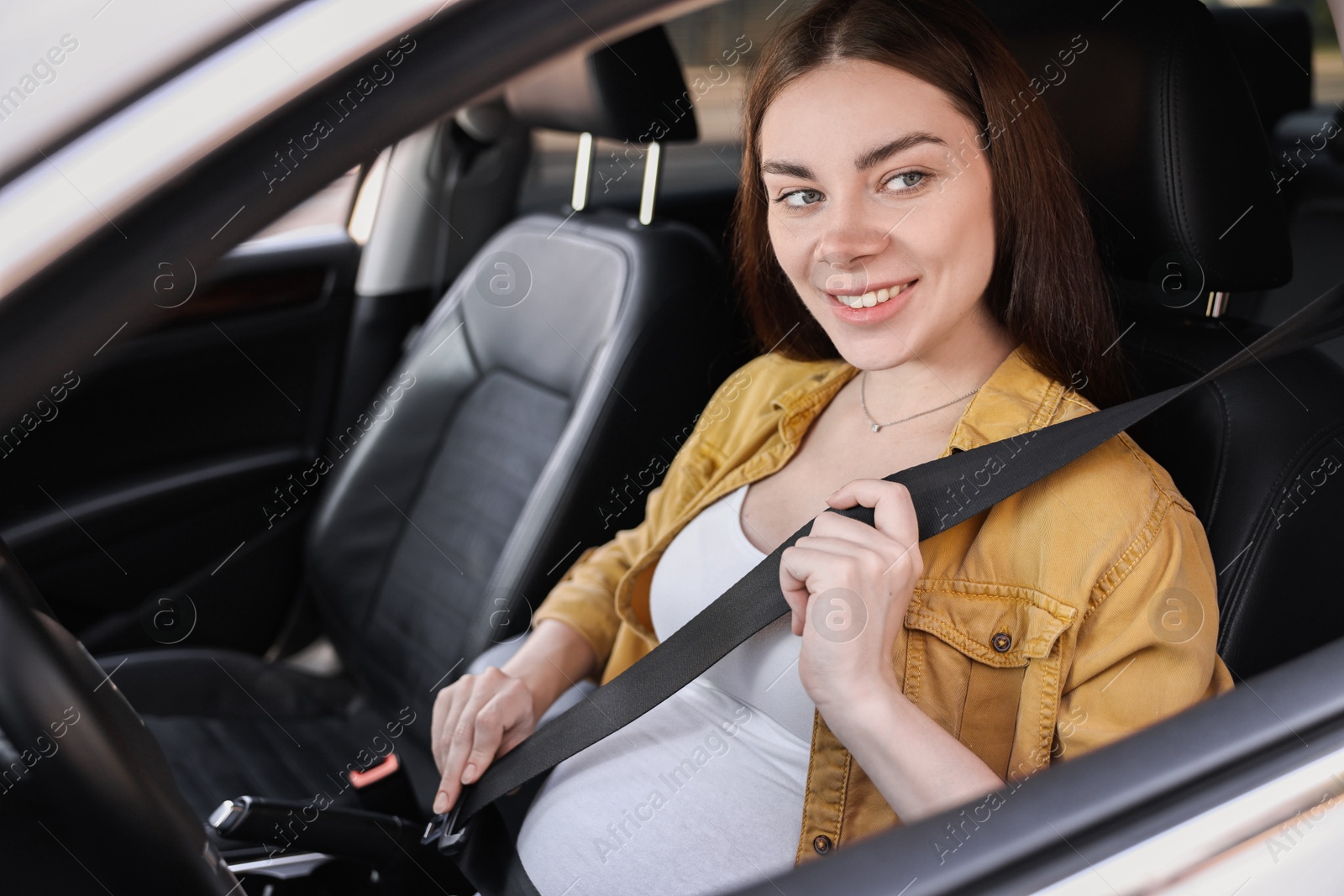 Photo of Smiling pregnant woman fastening safety belt in car, view from outside