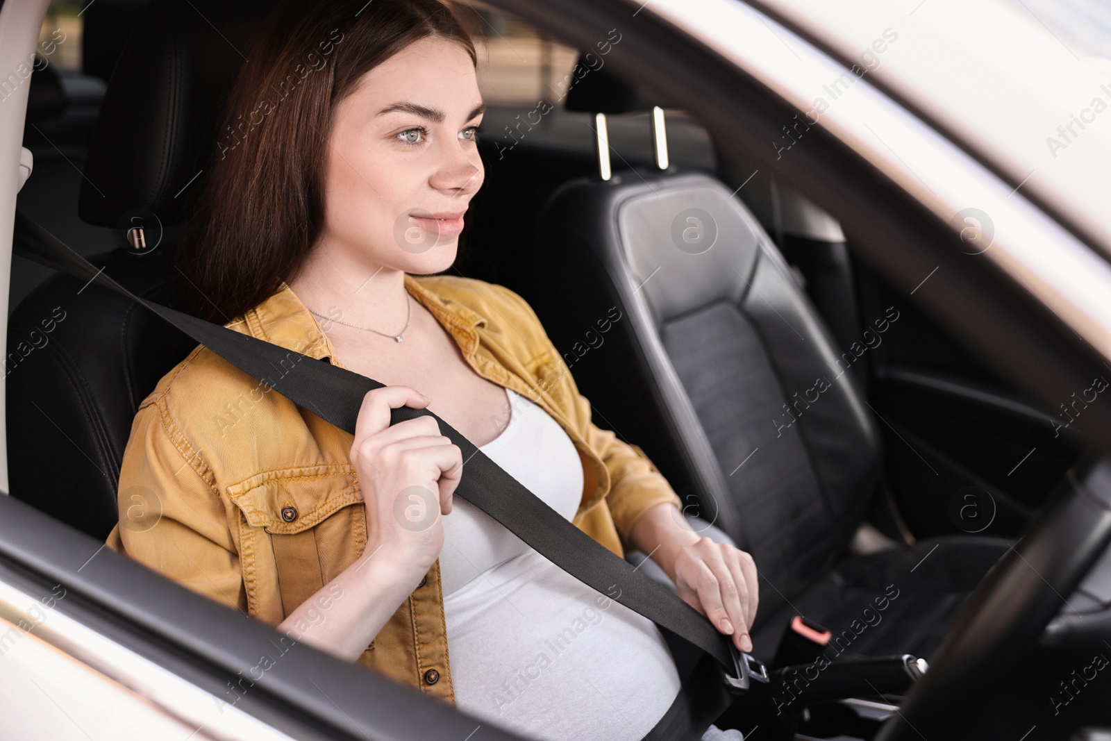 Photo of Pregnant woman fastening safety belt in car, view from outside