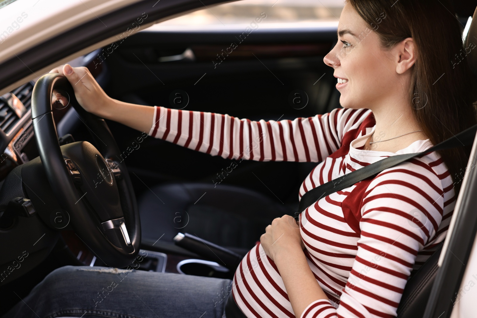 Photo of Smiling pregnant woman with safety belt driving car