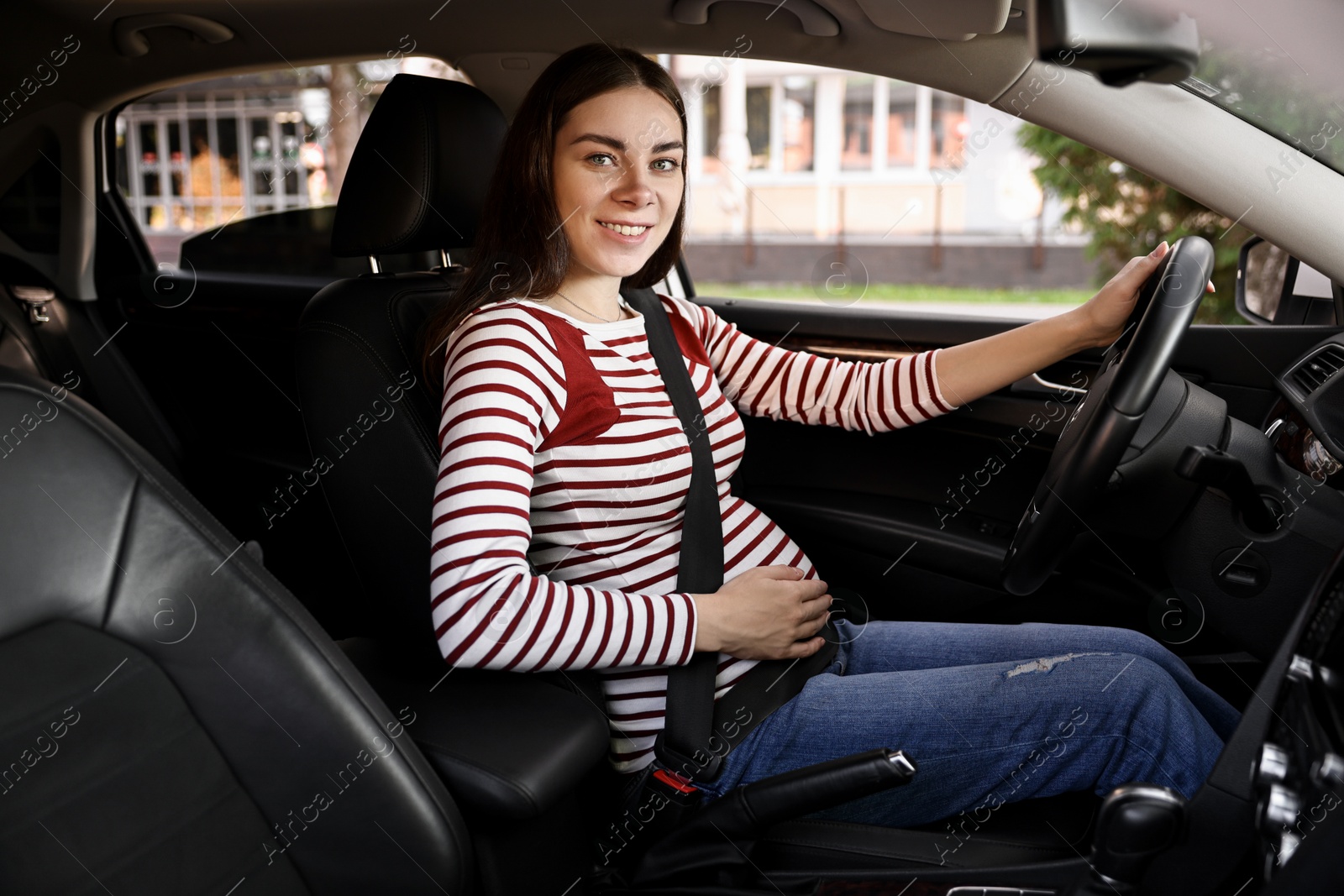 Photo of Smiling pregnant woman with safety belt driving car