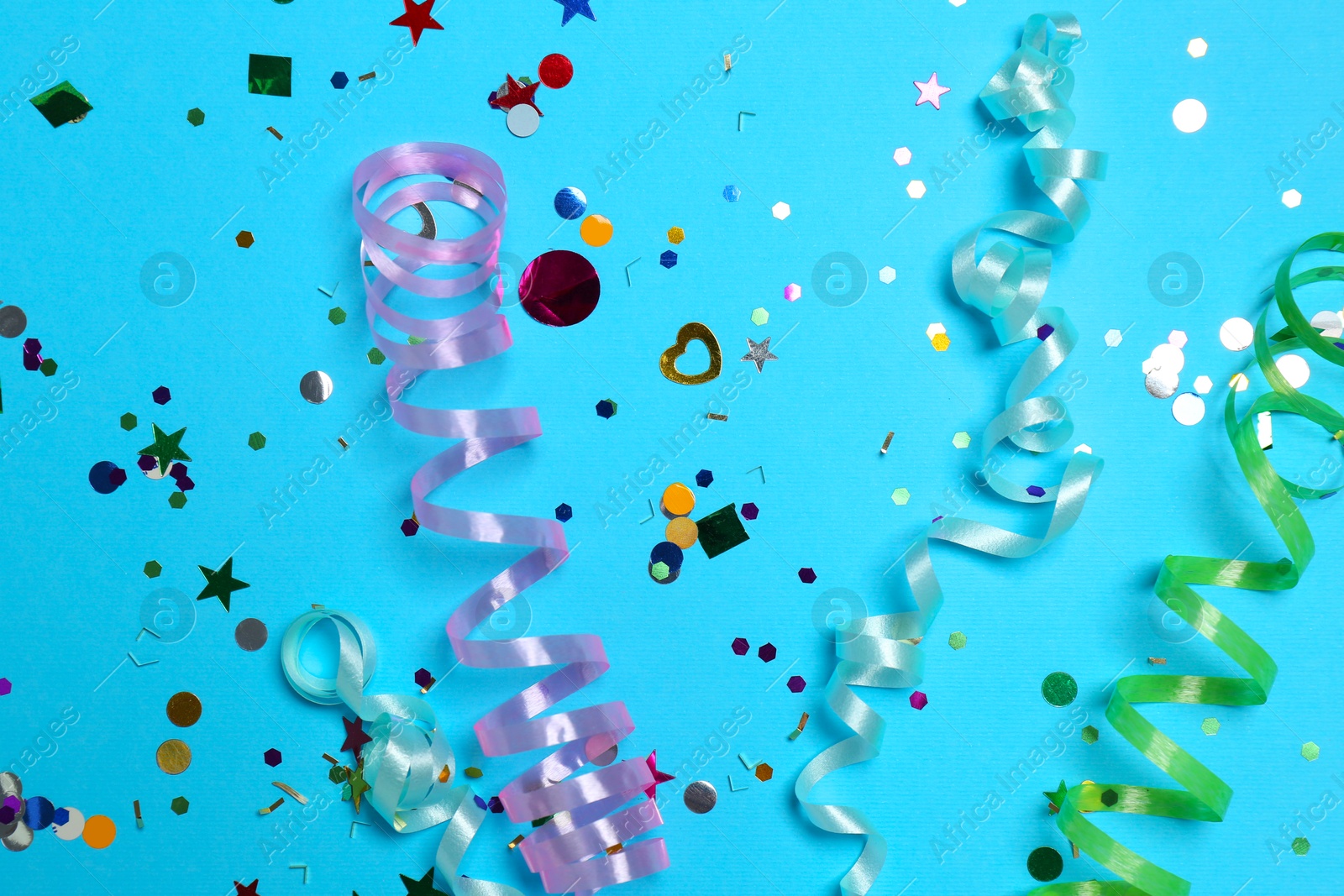 Photo of Shiny confetti and party streamers on light blue background, flat lay