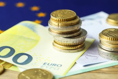 Photo of Euro banknotes, coins and European Union flag on table, closeup