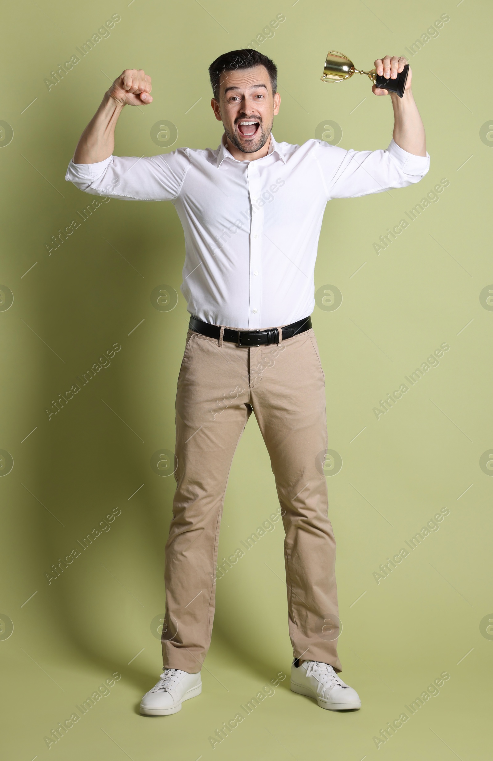 Photo of Happy winner with golden trophy cup on pale olive background