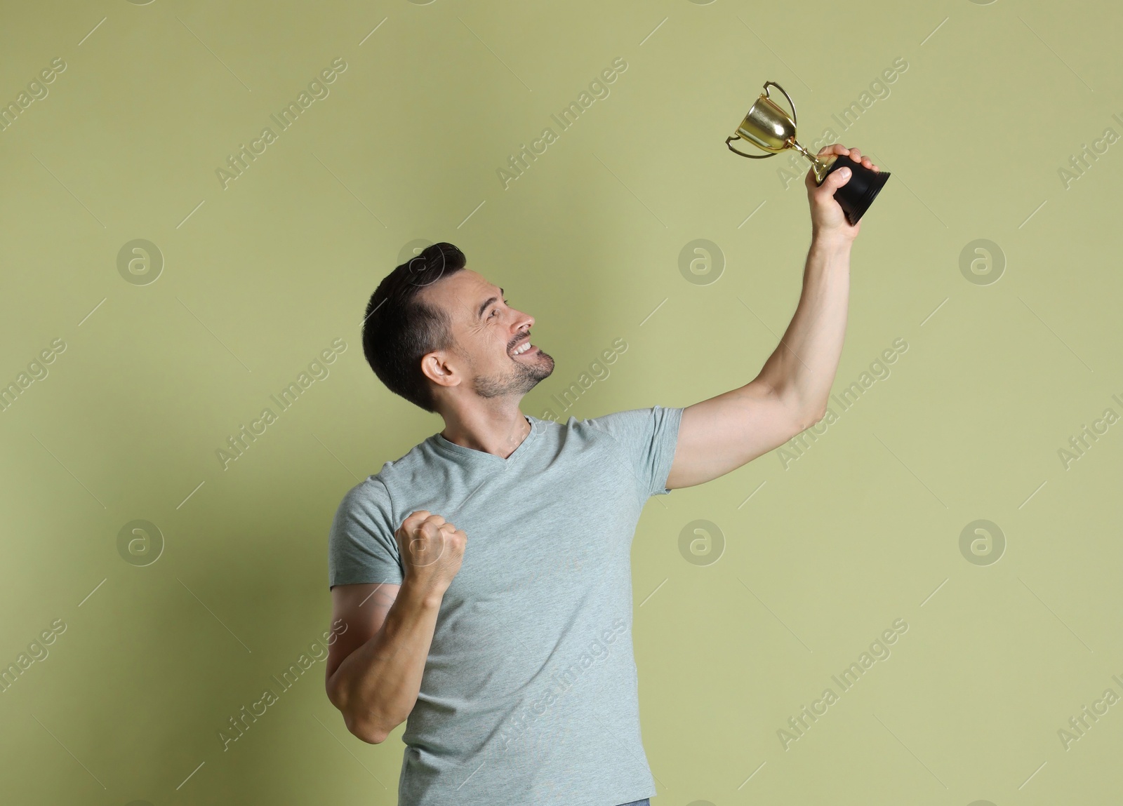 Photo of Happy winner with golden trophy cup on pale olive background