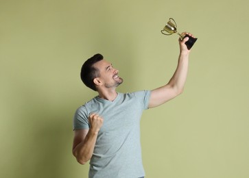 Happy winner with golden trophy cup on pale olive background