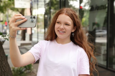 Beautiful teenage girl taking selfie with smartphone outdoors