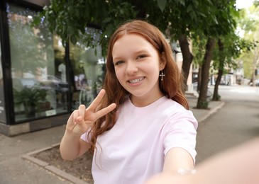 Beautiful teenage girl taking selfie on city street