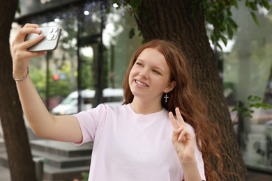 Photo of Beautiful teenage girl taking selfie with smartphone outdoors