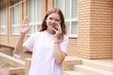 Beautiful teenage girl talking on phone and greeting someone outdoors