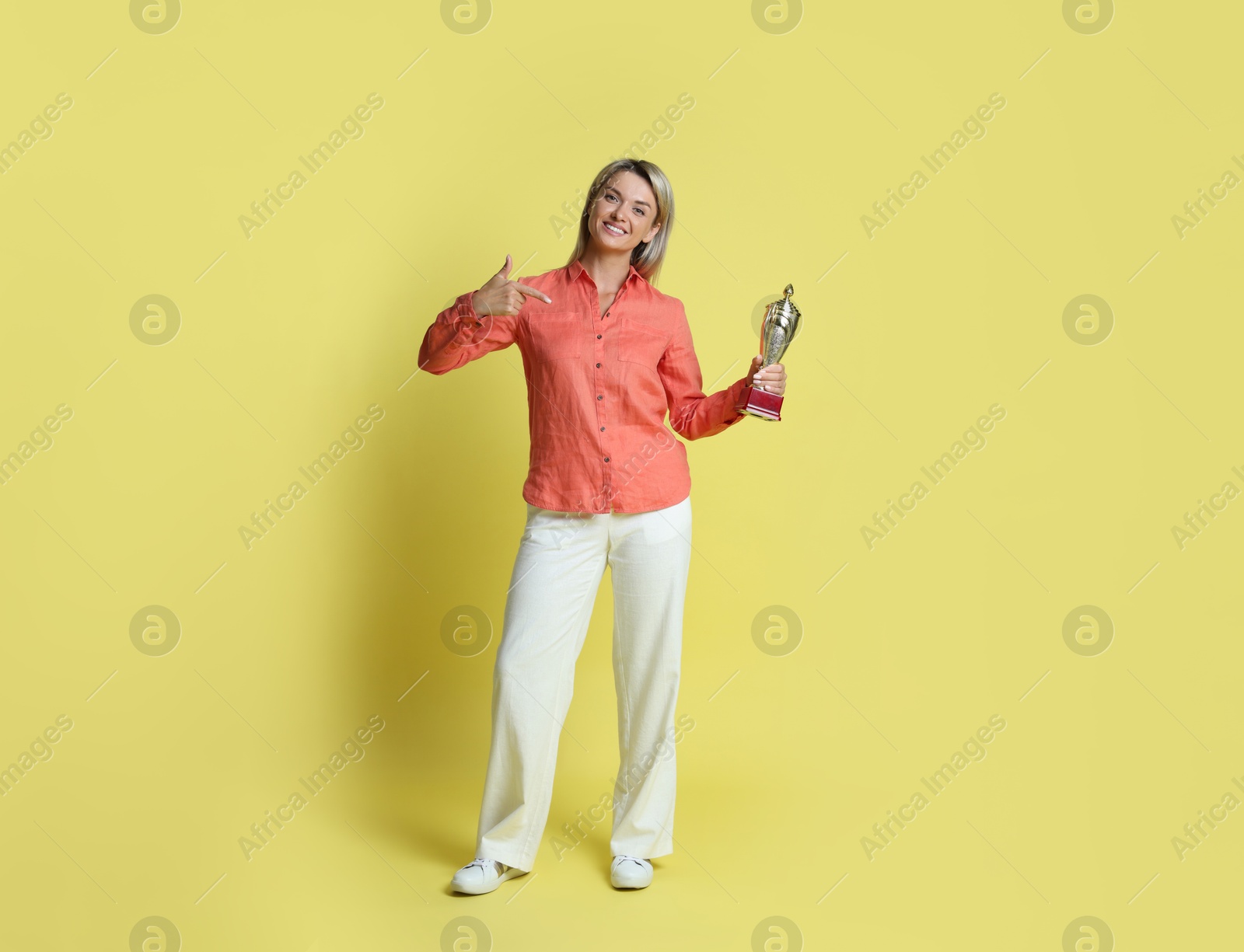 Photo of Happy winner with golden trophy cup on yellow background