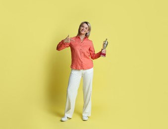 Photo of Happy winner with golden trophy cup on yellow background