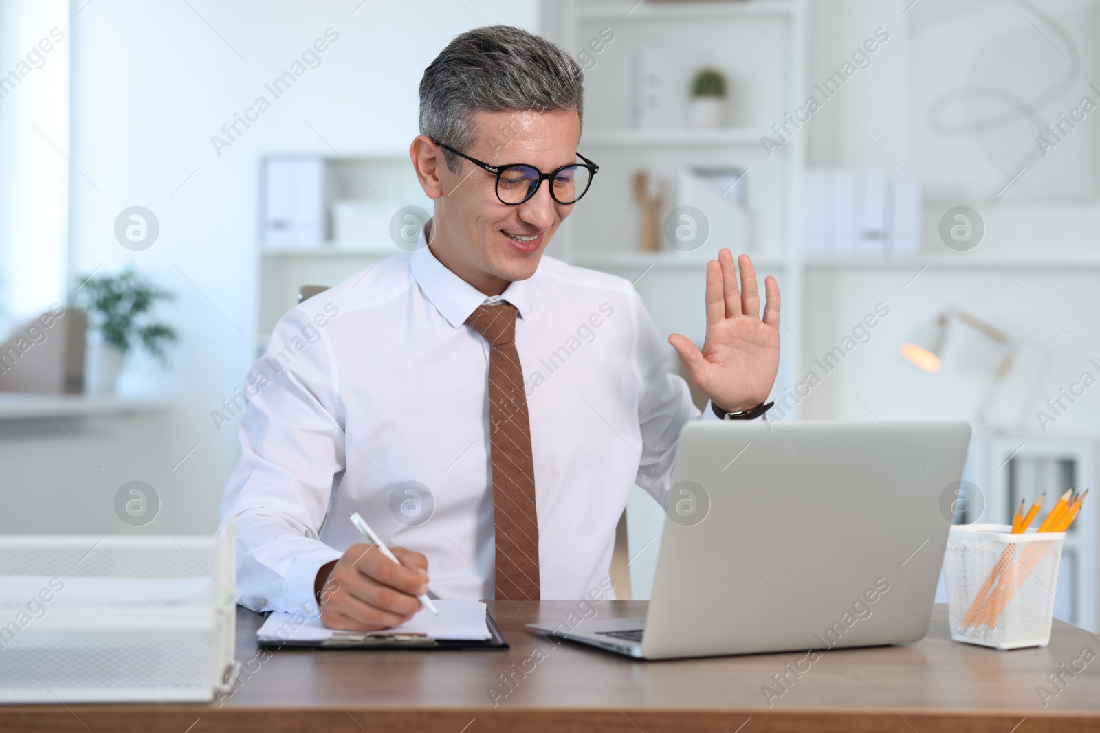 Photo of Smiling middle aged man having videochat via laptop at table in office