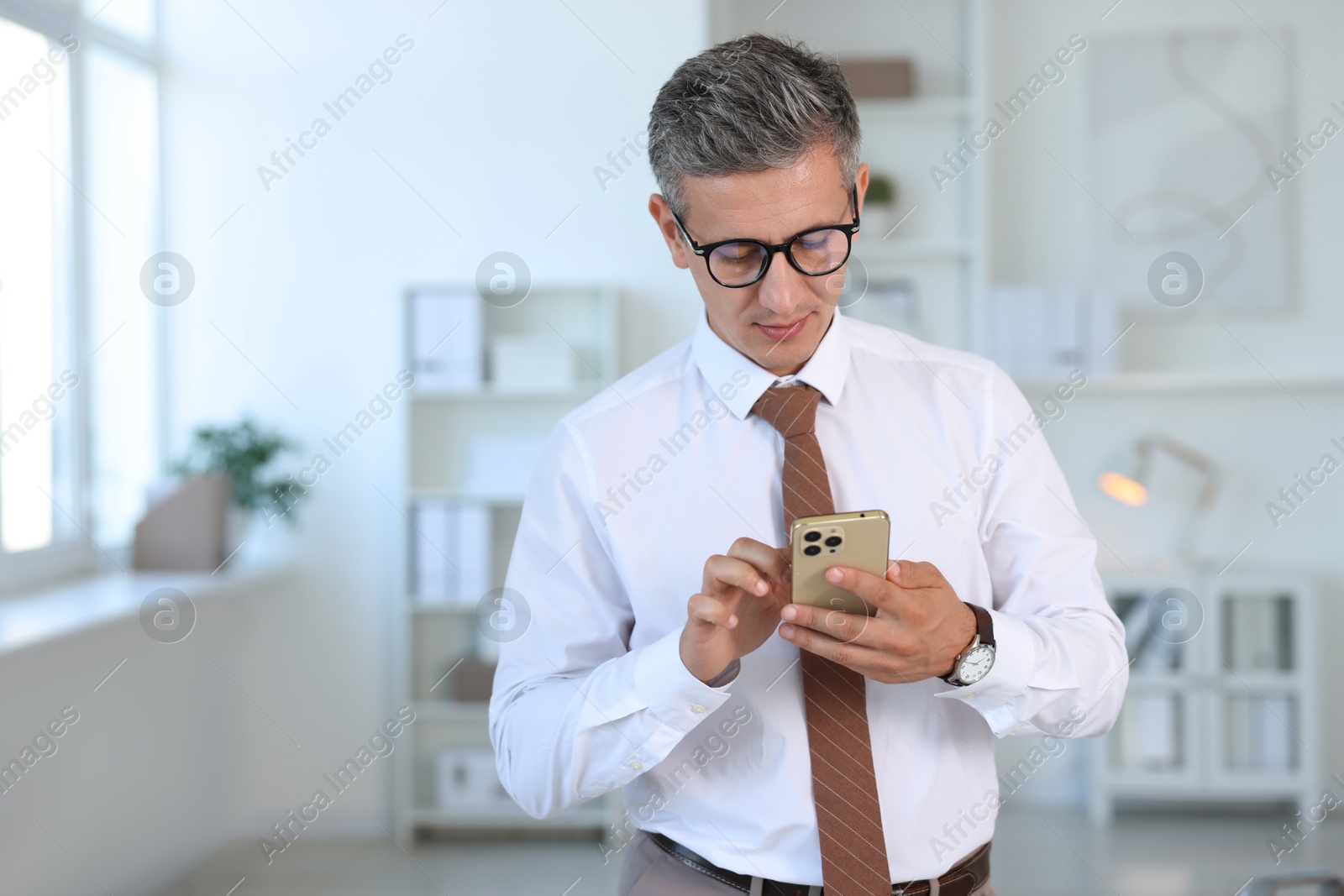 Photo of Middle aged man using smartphone in office. Space for text