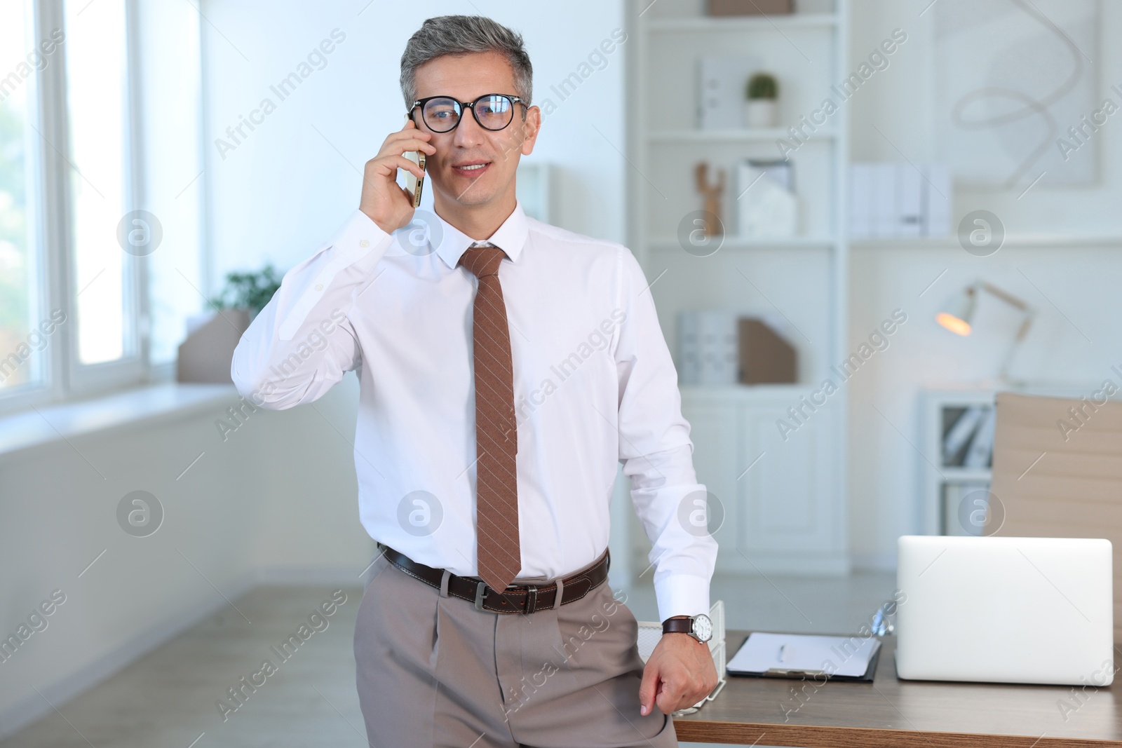 Photo of Middle aged man talking by smartphone in office