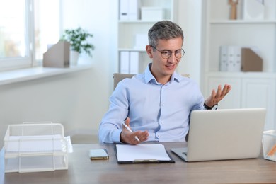 Photo of Middle aged man having videochat by laptop at table in office