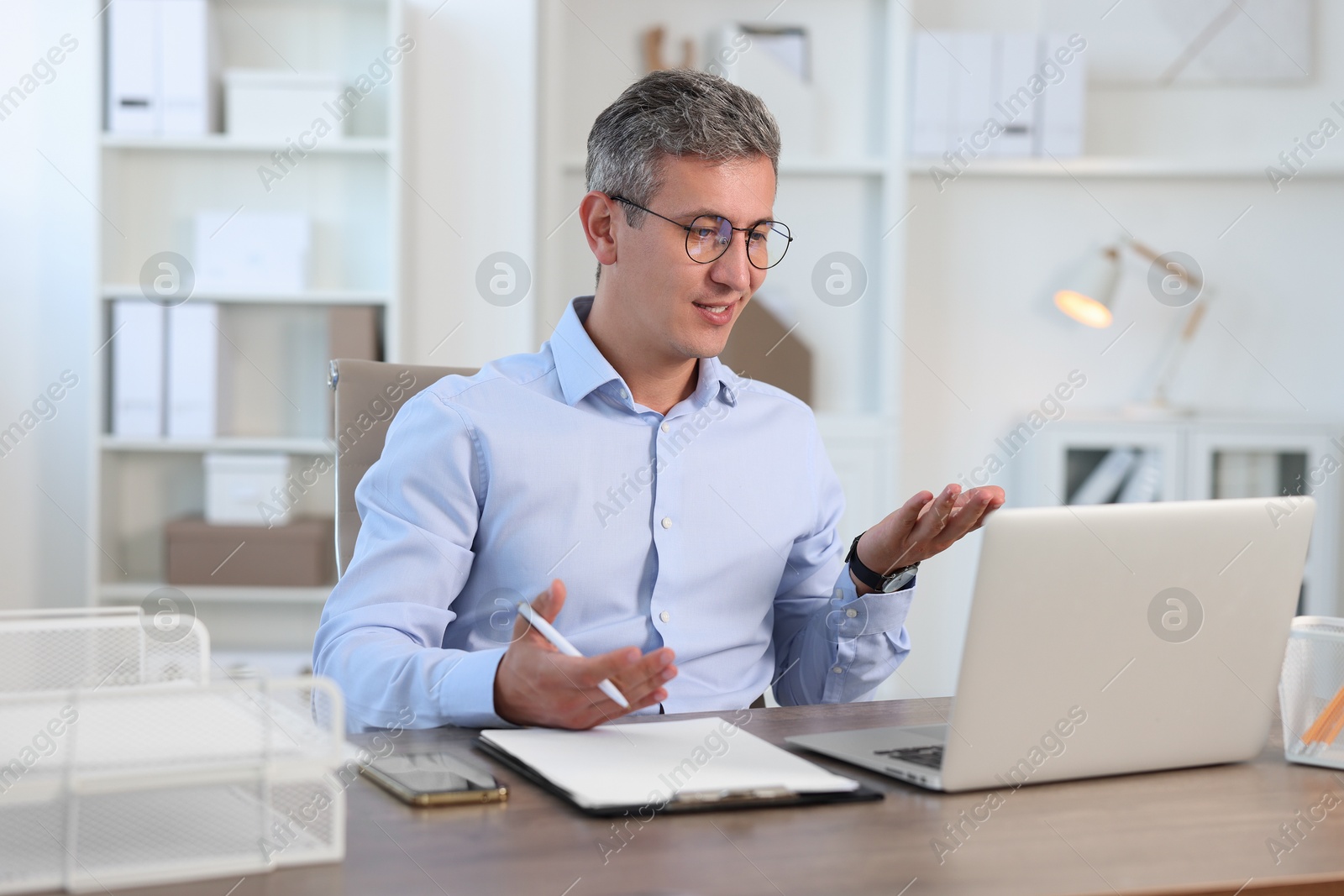 Photo of Middle aged man having videochat by laptop at table in office