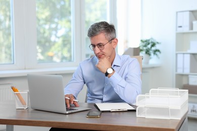 Photo of Middle aged man working with laptop at table in office