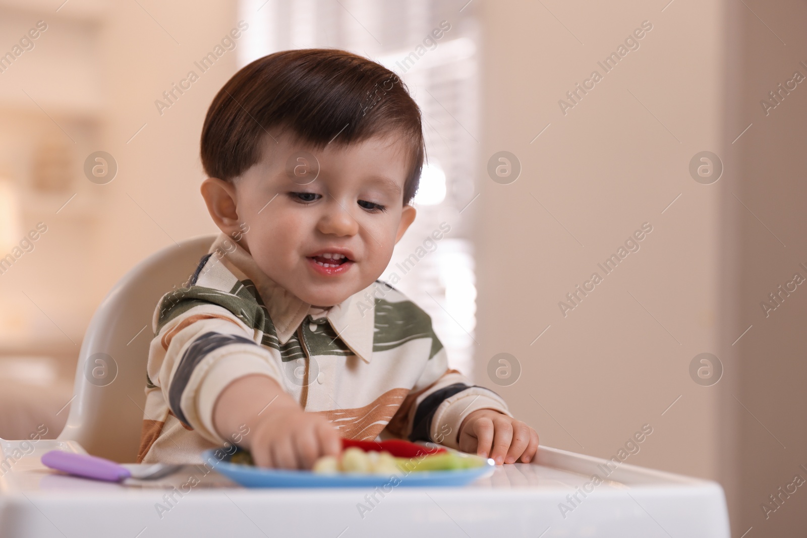 Photo of Cute little baby eating healthy food in high chair at home