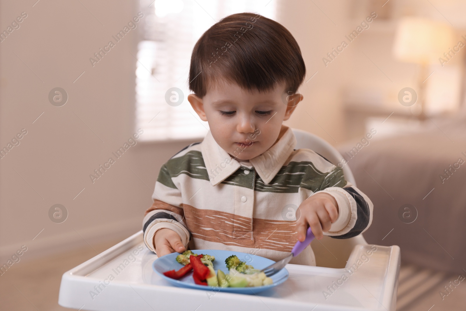 Photo of Cute little baby eating healthy food in high chair at home