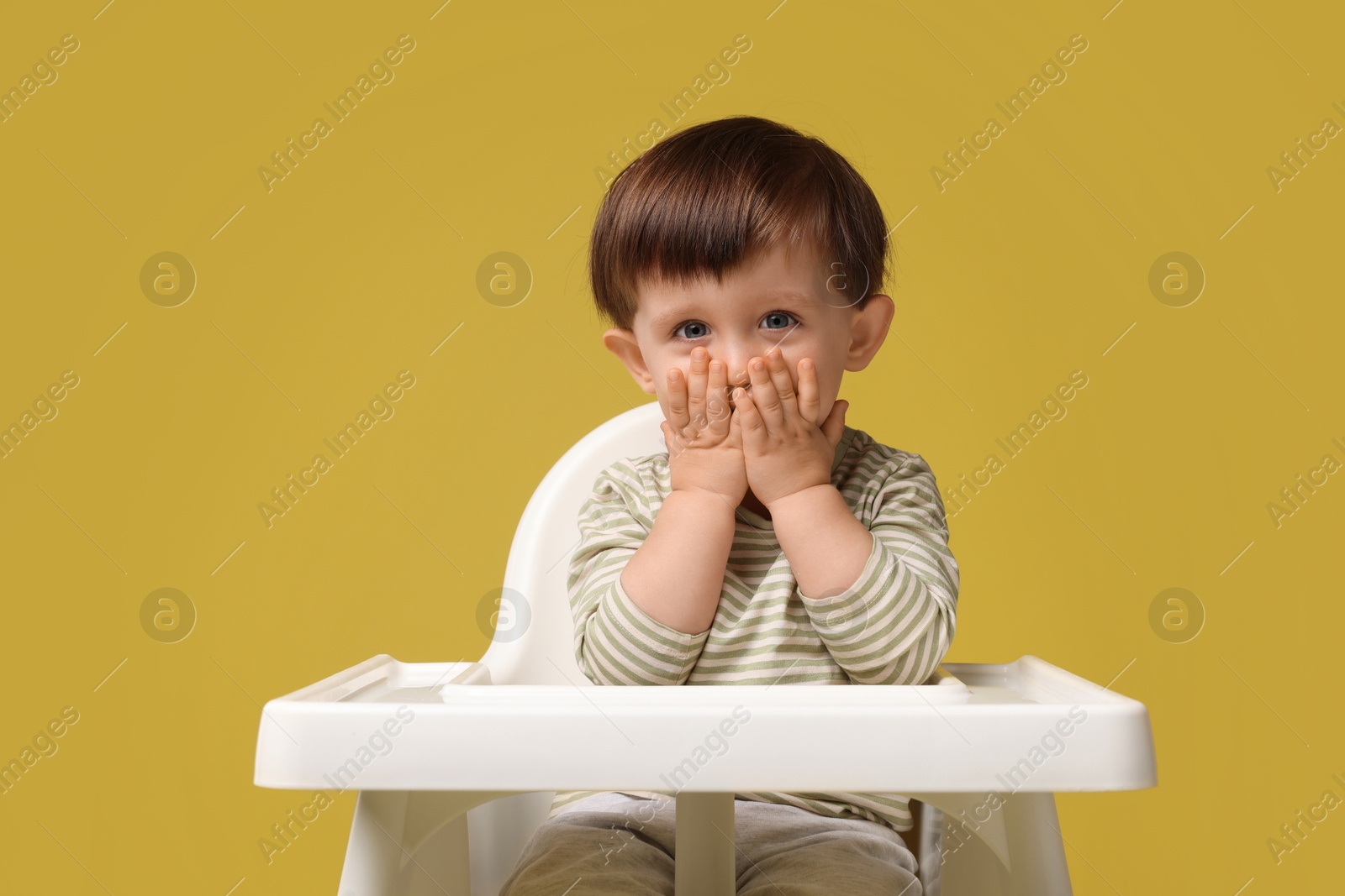 Photo of Cute little kid sitting in high chair on yellow background