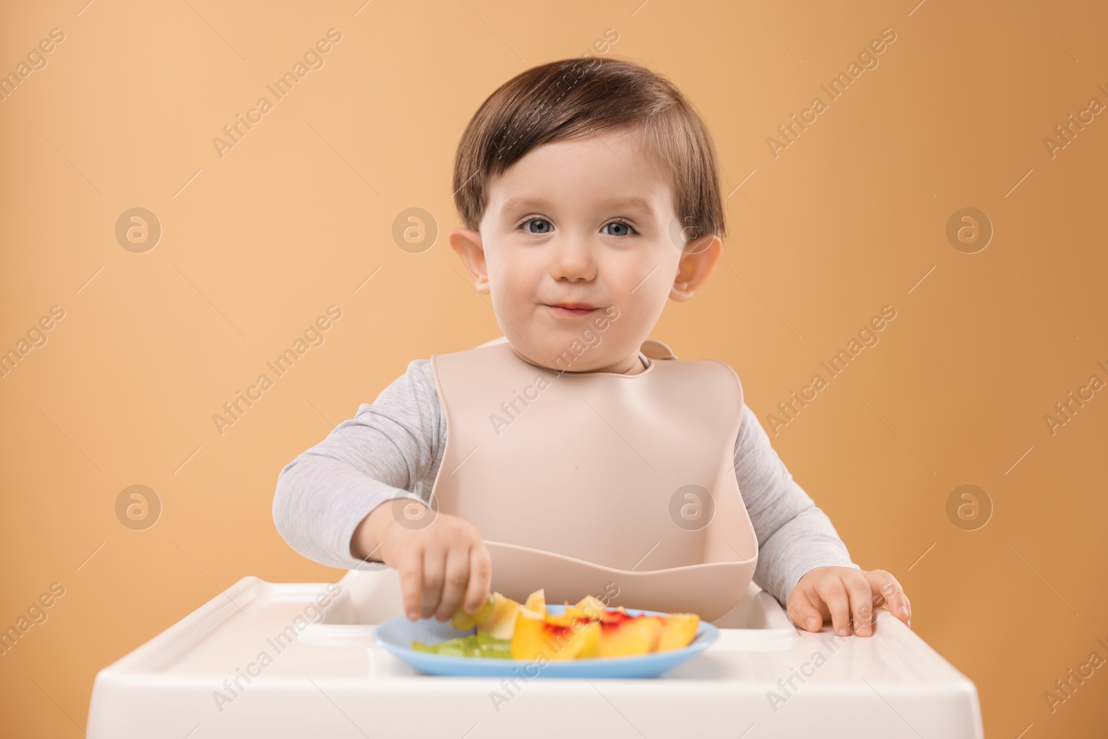 Photo of Healthy baby food. Cute little kid eating fruits in high chair on beige background