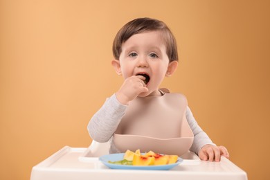 Photo of Healthy baby food. Cute little kid eating fruits in high chair on beige background