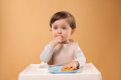 Photo of Healthy baby food. Cute little kid eating fruits in high chair on beige background