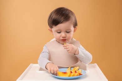 Photo of Healthy baby food. Cute little kid eating fruits in high chair on beige background