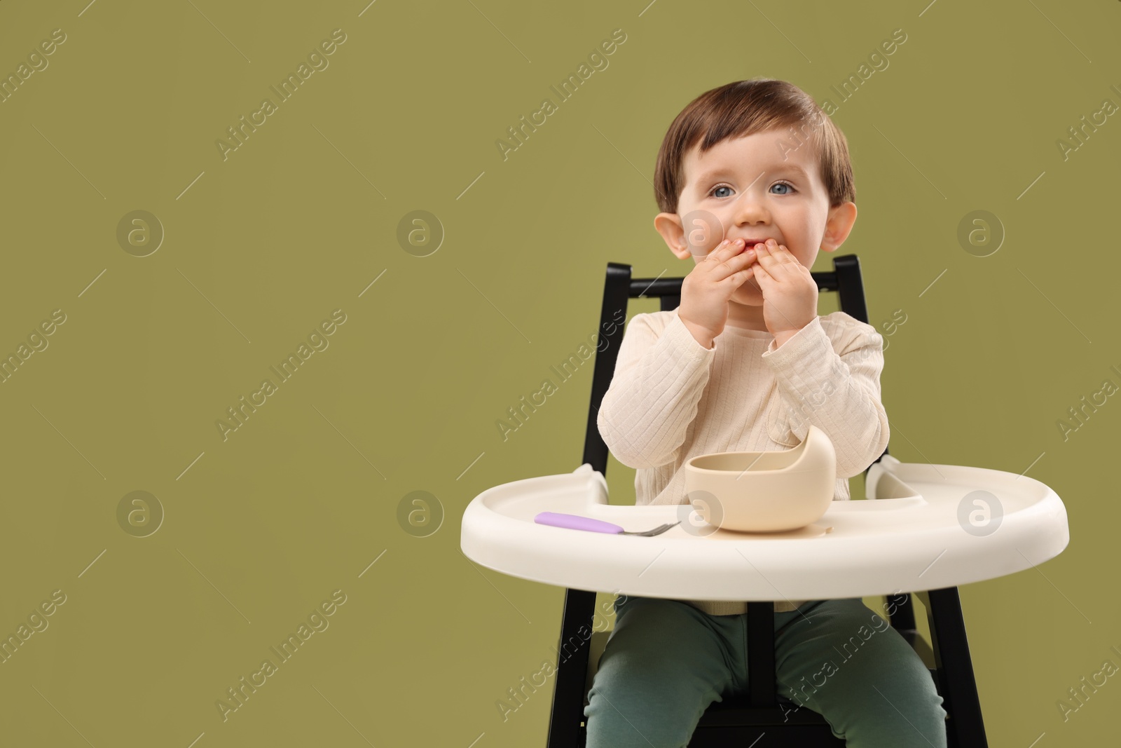 Photo of Cute little baby eating healthy food from bowl in high chair on olive background, space for text