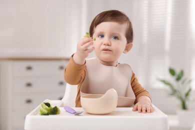 Photo of Cute little baby eating healthy food from bowl in high chair at home