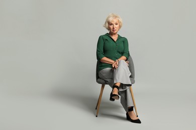 Photo of Beautiful senior woman sitting on chair against light grey background, space for text