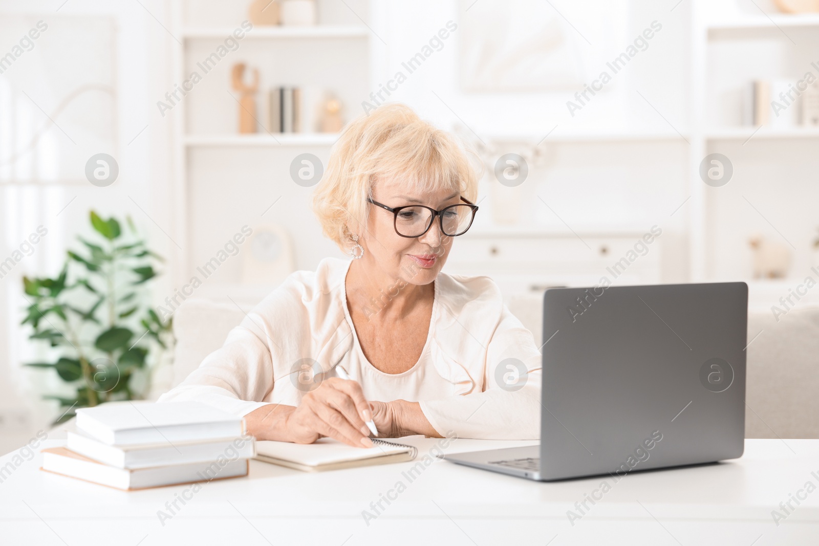 Photo of Beautiful senior woman using laptop at white table indoors