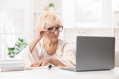 Photo of Beautiful senior woman using laptop at white table indoors