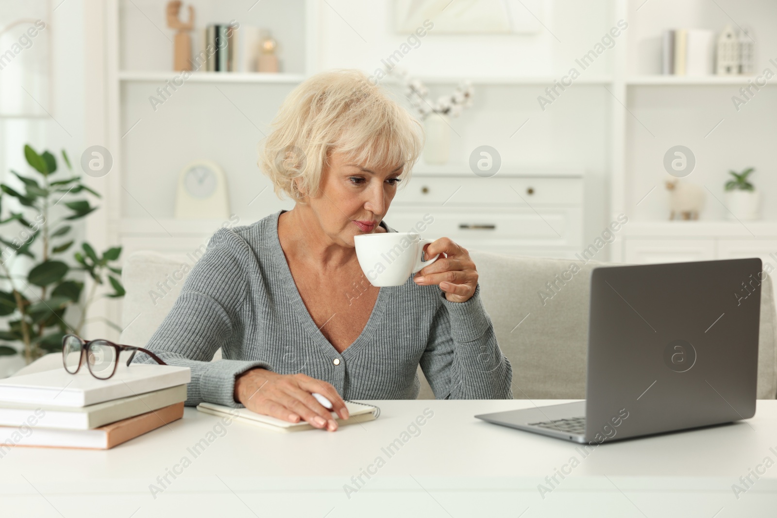 Photo of Beautiful senior woman using laptop at white table indoors