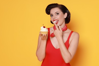 Photo of Pin-up woman eating cupcake on orange background, space for text