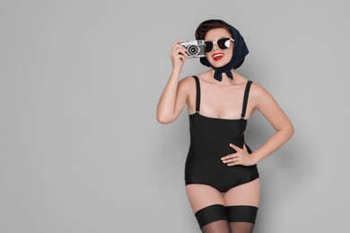 Pin-up woman in sunglasses with camera on grey background, space for text