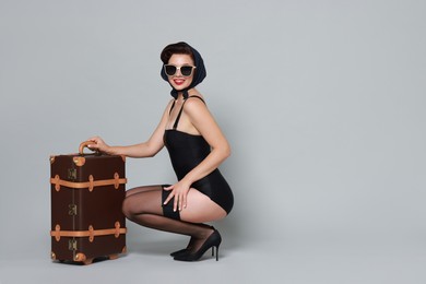 Pin-up woman with suitcase on grey background, space for text