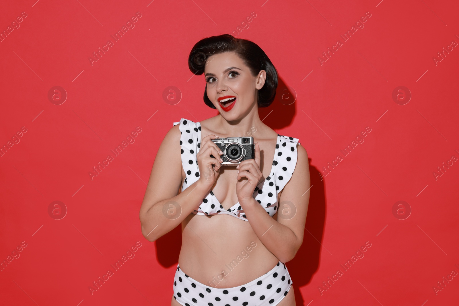 Photo of Pin-up woman in bikini with camera on red background