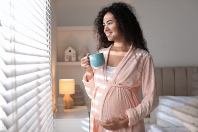 Photo of Portrait of beautiful pregnant with cup of drink near window at home