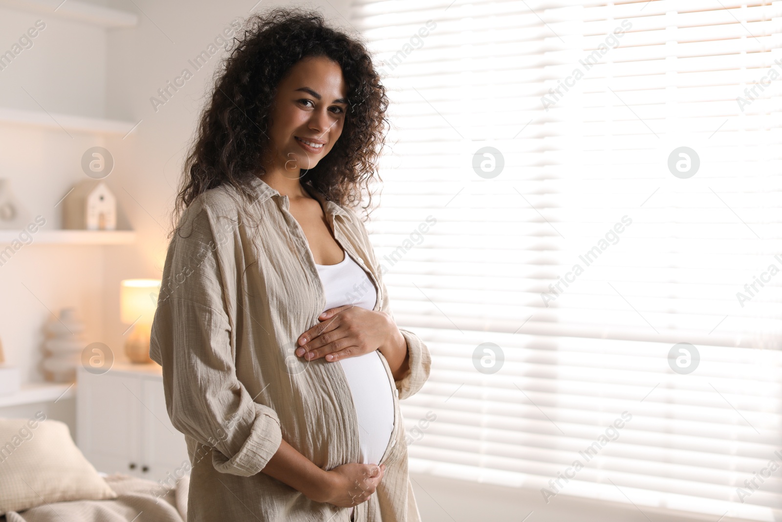 Photo of Portrait of beautiful pregnant woman near window at home, space for text