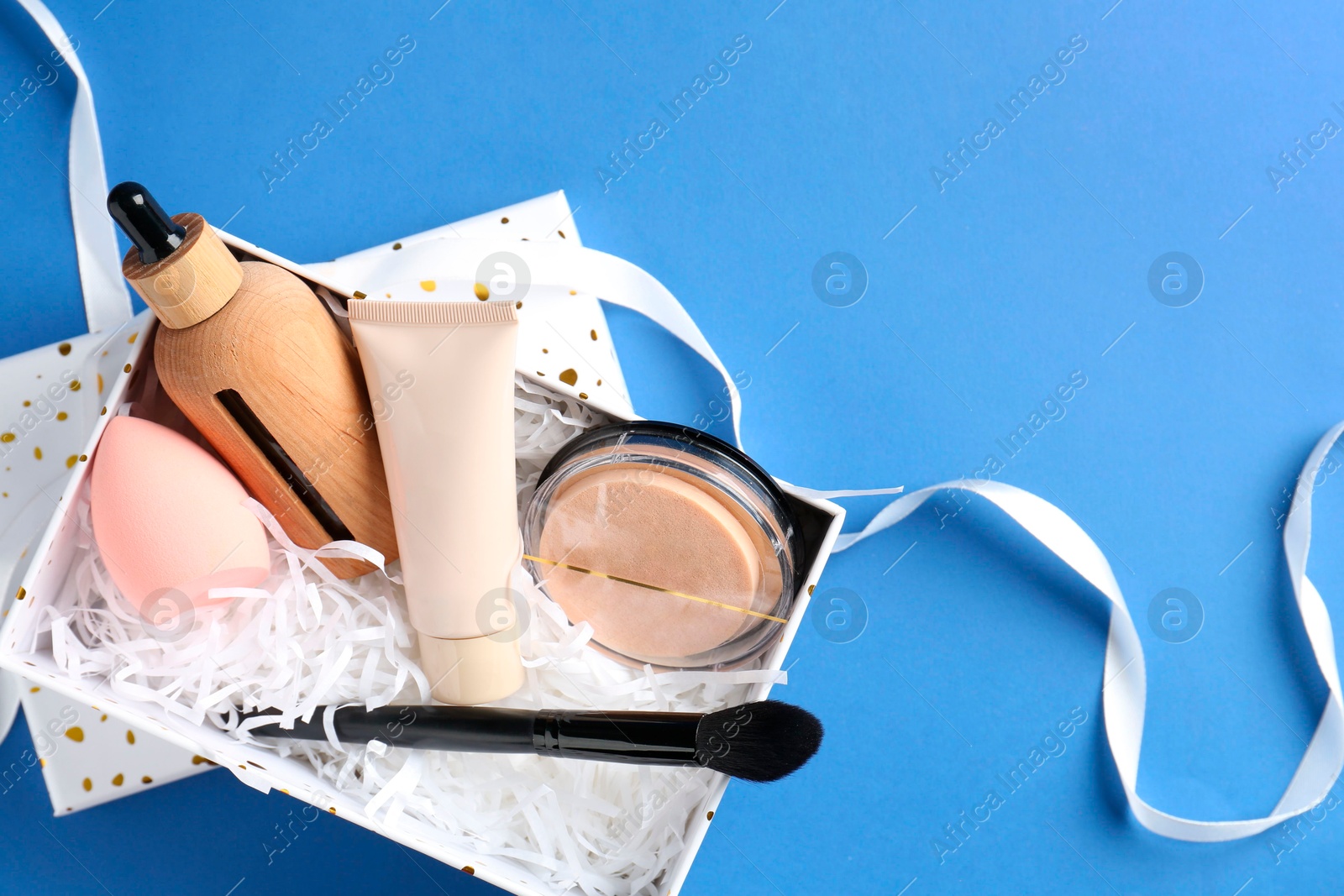 Photo of Cosmetic products in gift box on blue background, top view. Space for text