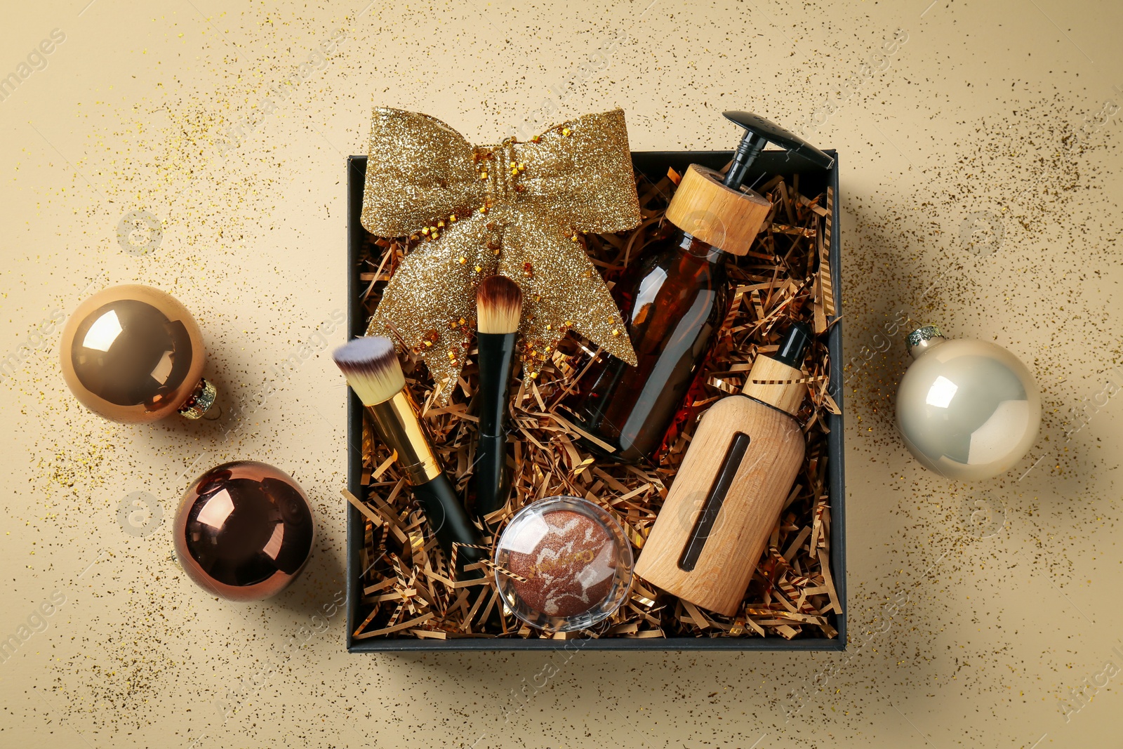 Photo of Christmas gift box with cosmetic products and festive balls on beige background, flat lay