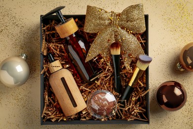 Christmas gift box with cosmetic products and festive balls on beige background, flat lay