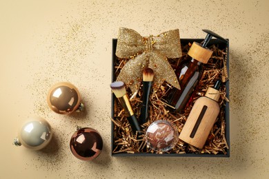 Photo of Christmas gift box with cosmetic products and festive balls on beige background, flat lay