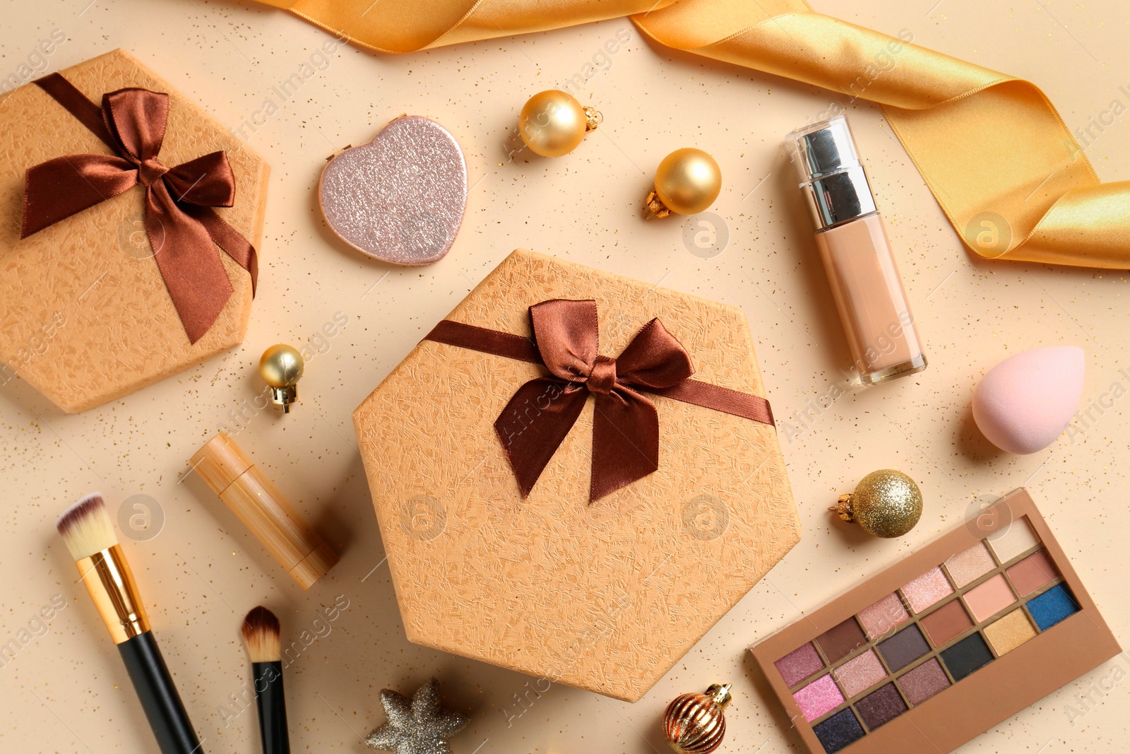 Photo of Decorative cosmetics as Christmas present. Makeup products, gift boxes and festive balls on beige background, flat lay