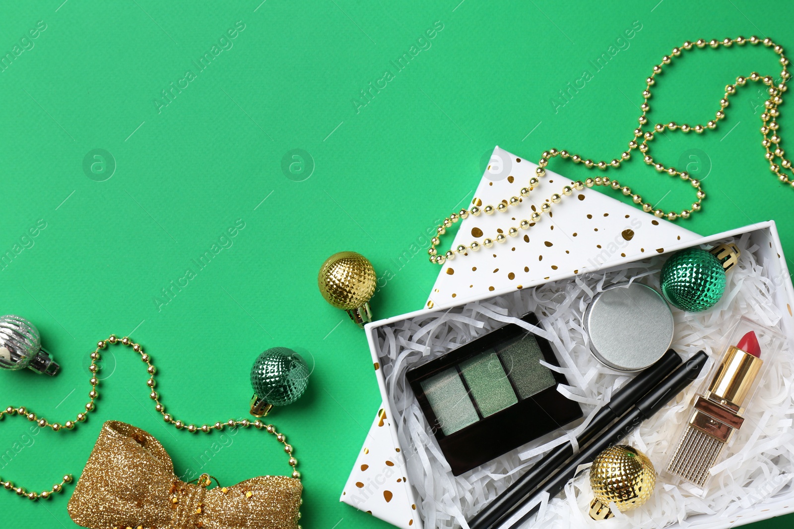 Photo of Christmas gift box with decorative cosmetics and festive ornaments on green background, flat lay. Space for text