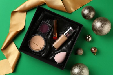 Photo of Christmas present. Decorative cosmetics in gift box and festive balls on green background, flat lay